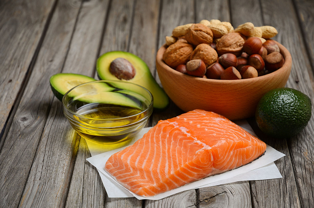 Gary Brecka's diet includes a spread of salmon, avocado, nuts, and olive oil on a wooden table. A wholesome meal option.