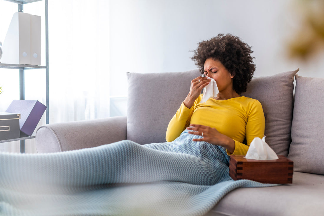 A woman sitting on a couch with a tissue in her hand, possibly due to seasonal allergies.