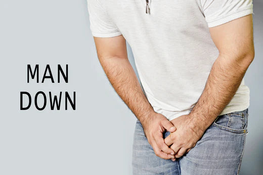 A man in white shirt and blue jeans with his hand over private part concerned about erectile dysfunction