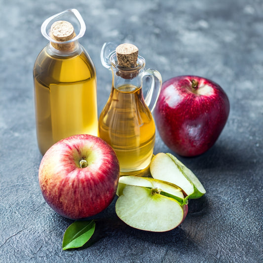 Two bottles of apple cider vinegar and two red apples along with 2 half of green apple on dark surface