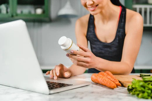 A woman holding a bottle of vitamins and a laptop, supplements for digestive health.
