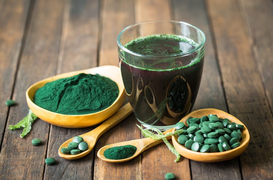 Green powder in a glass and green pills in a bowl, showcasing the advantages of Chlorella supplements