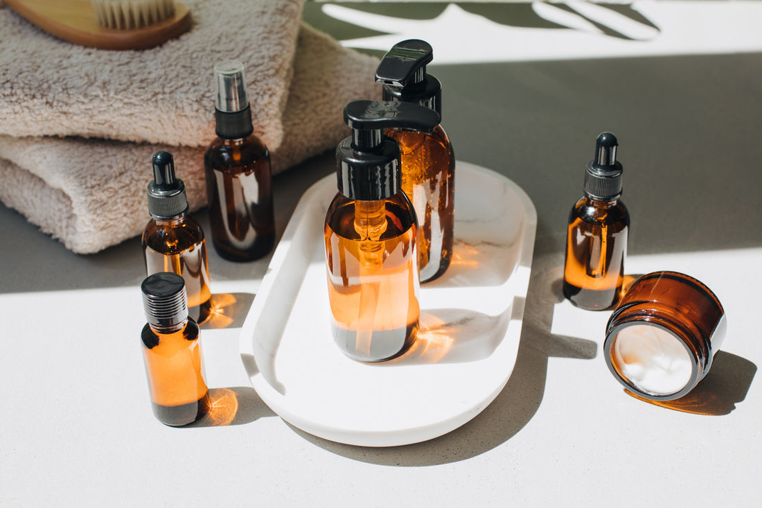 Amber bottles with facial treatment on a white tray with green leaves on backdrop