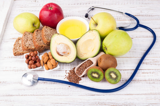 Assortment of cholesterol lowering foods displayed with stethoscope on white wooden table.