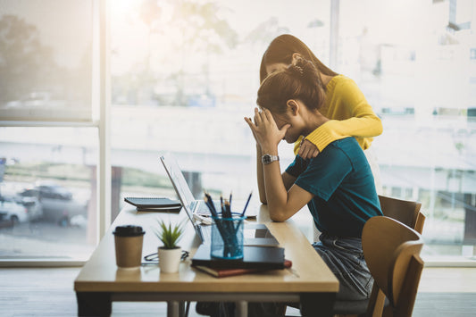 A woman sitting at a desk with a hand on her shoulder. Self-care tips: balancing work and personal life.