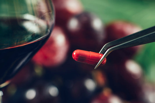 Hand holding resveratrol supplement near wine glass