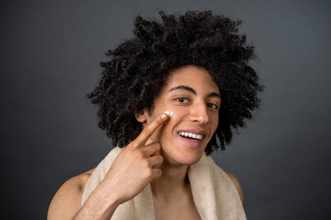 Skin care. Smiling guy with towel on his neck applying face cream