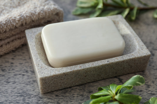 Dish tea tree soap bar, terry towel and green plants on light grey textured table.