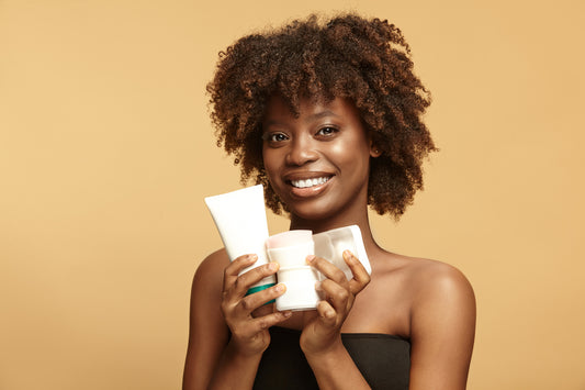 Smiling black skinned woman with a natural clean skin and afro style hair demonstrating few skincare products  for rosacea relief