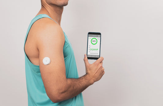 A man holding a smartphone with a monitor displaying blood sugar levels.