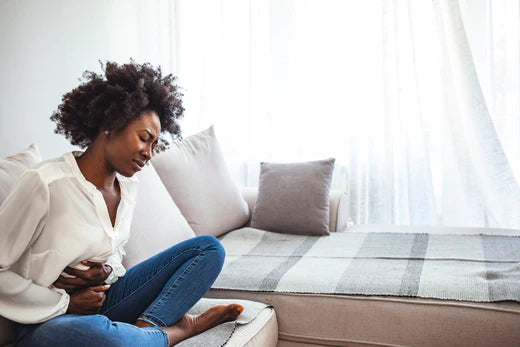 A woman on a couch, clutching her stomach in pain, possibly due to acid reflux.